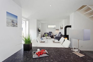 Un salon moderne avec une cheminée, un coin repas avec une table dressée pour deux personnes et un espace cuisine équipé d’une cuisinière.