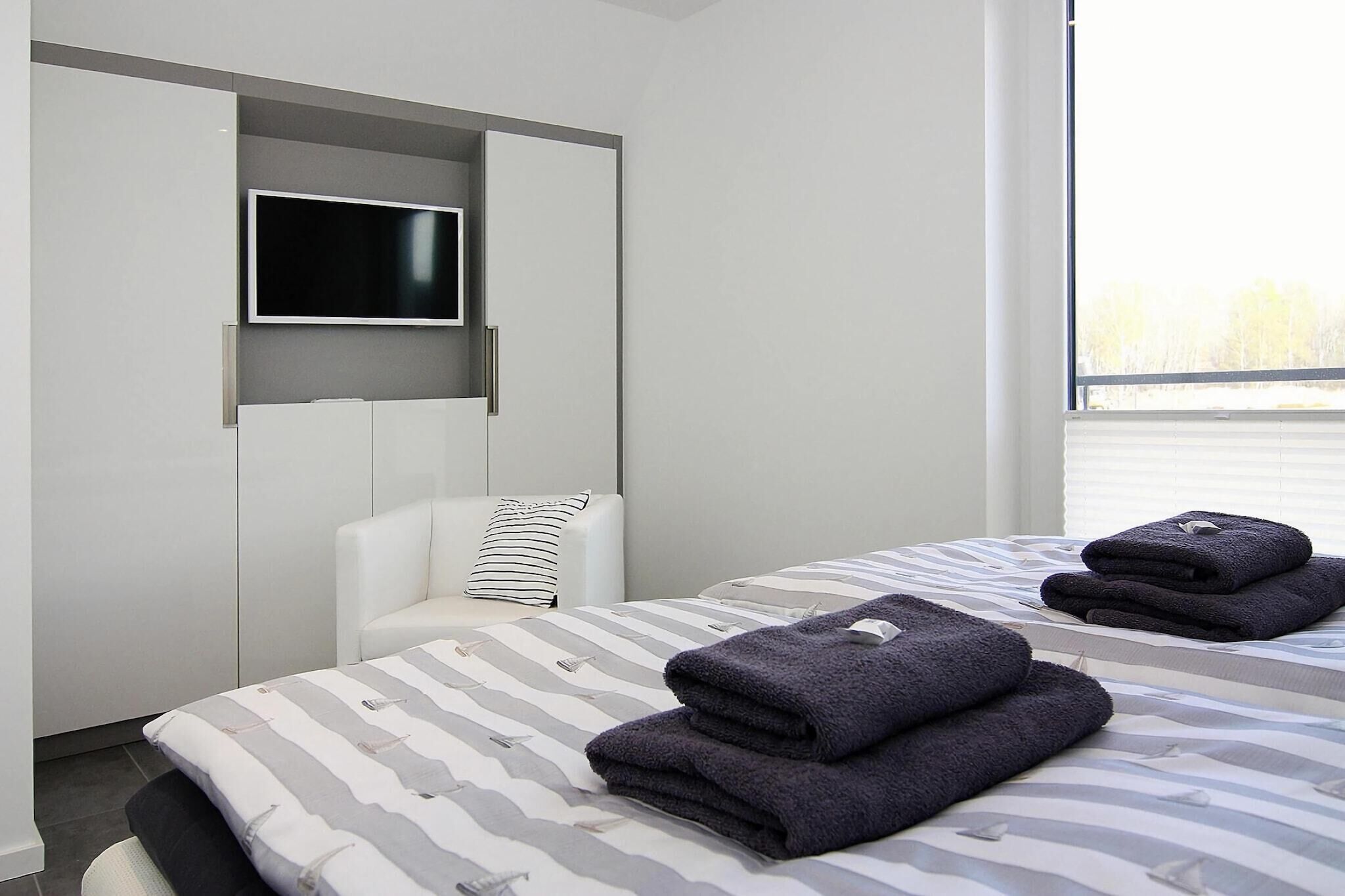 A modern hotel room with a bed, a TV mounted on a wall, and a window providing a view of the outdoors.