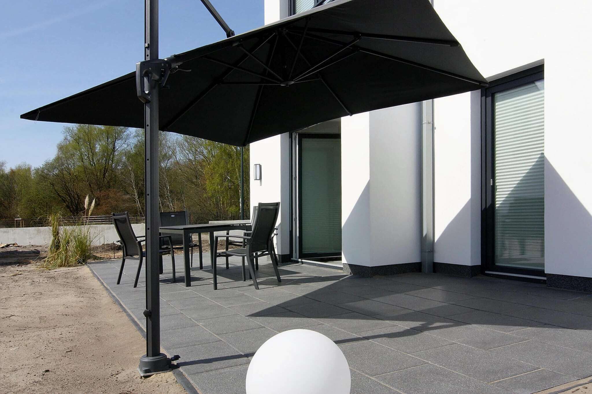 An outdoor patio with a table and chairs, a black umbrella, and a white spherical decoration.
