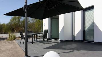 An outdoor patio with a table and chairs, a black umbrella, and a white spherical decoration.