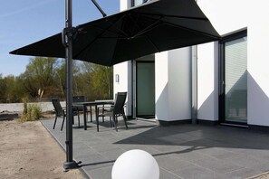 En udendørs terrasse med et bord, stole og en sort parasol samt en rund, hvid dekoration.