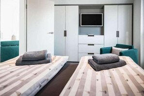 Une chambre moderne avec deux lits, une télévision et une armoire.