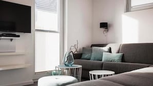 Una sala de estar moderna con un sofá gris, un televisor de pantalla plana y un florero de vidrio sobre una mesita blanca.