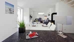 Ein modernes Wohnzimmer mit Kamin, einem Essbereich mit Tisch für zwei Personen und einer Küchenzeile mit Herd.