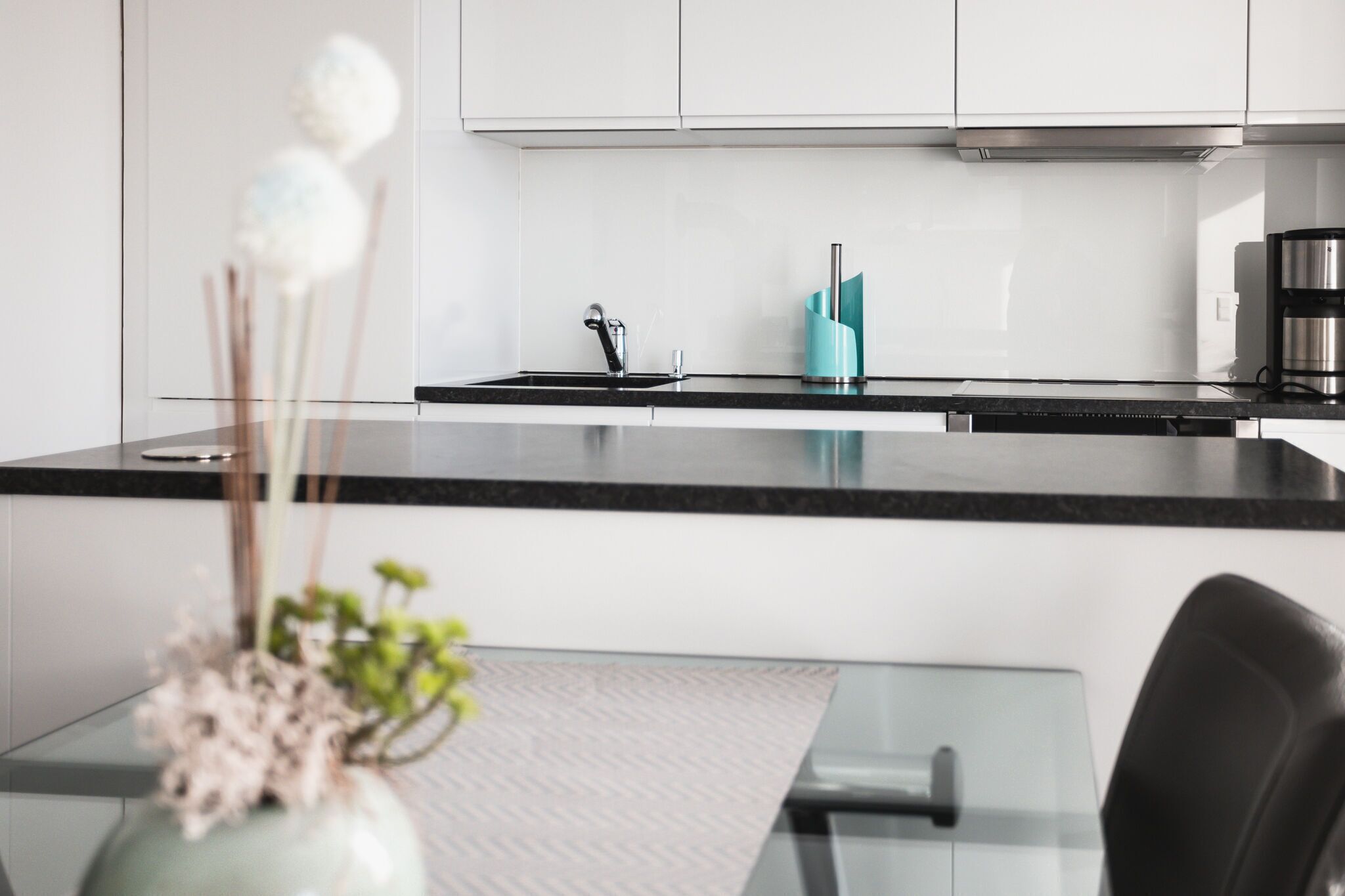 Una cocina moderna con armarios blancos, encimera negra y cafetera de acero inoxidable.