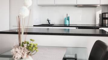 Una cocina moderna con armarios blancos, encimera negra y cafetera de acero inoxidable.