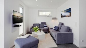 Ein modernes Wohnzimmer mit einem Flachbildfernseher, zwei grauen Sofas, einem weißen Couchtisch und einem großen Fenster.
