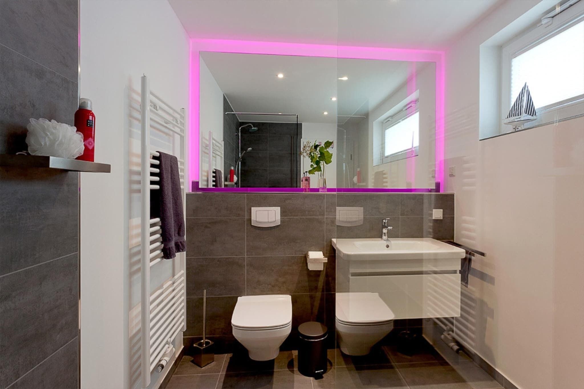 A modern bathroom with two toilets, a sink, and a shower.