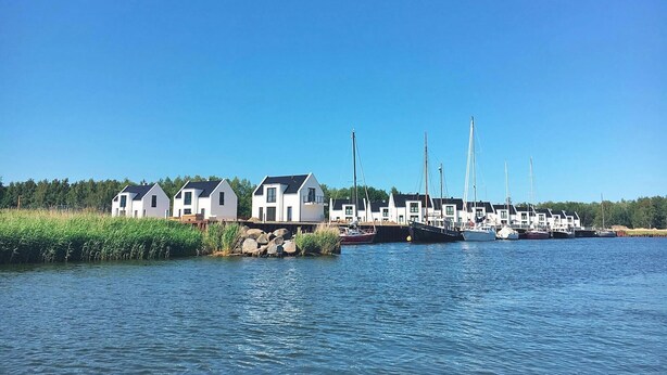 A waterfront property with several white houses, a dock with sailboats, and a calm lake.