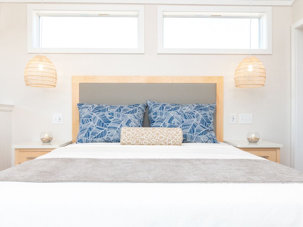 A bedroom with a large bed, two bedside tables, a wooden headboard, and two hanging lamps.