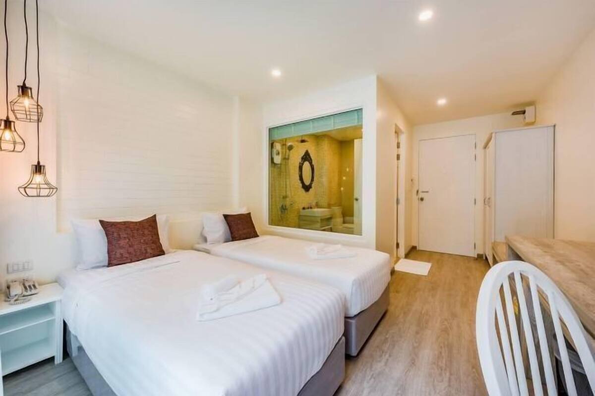A hotel room with two beds, a mirror, a white chair, and a small table.
