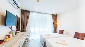 A hotel room with a bed, bedside tables, a desk, a television, and a window with curtains. - LullaBella Hotel Patong (Patong)