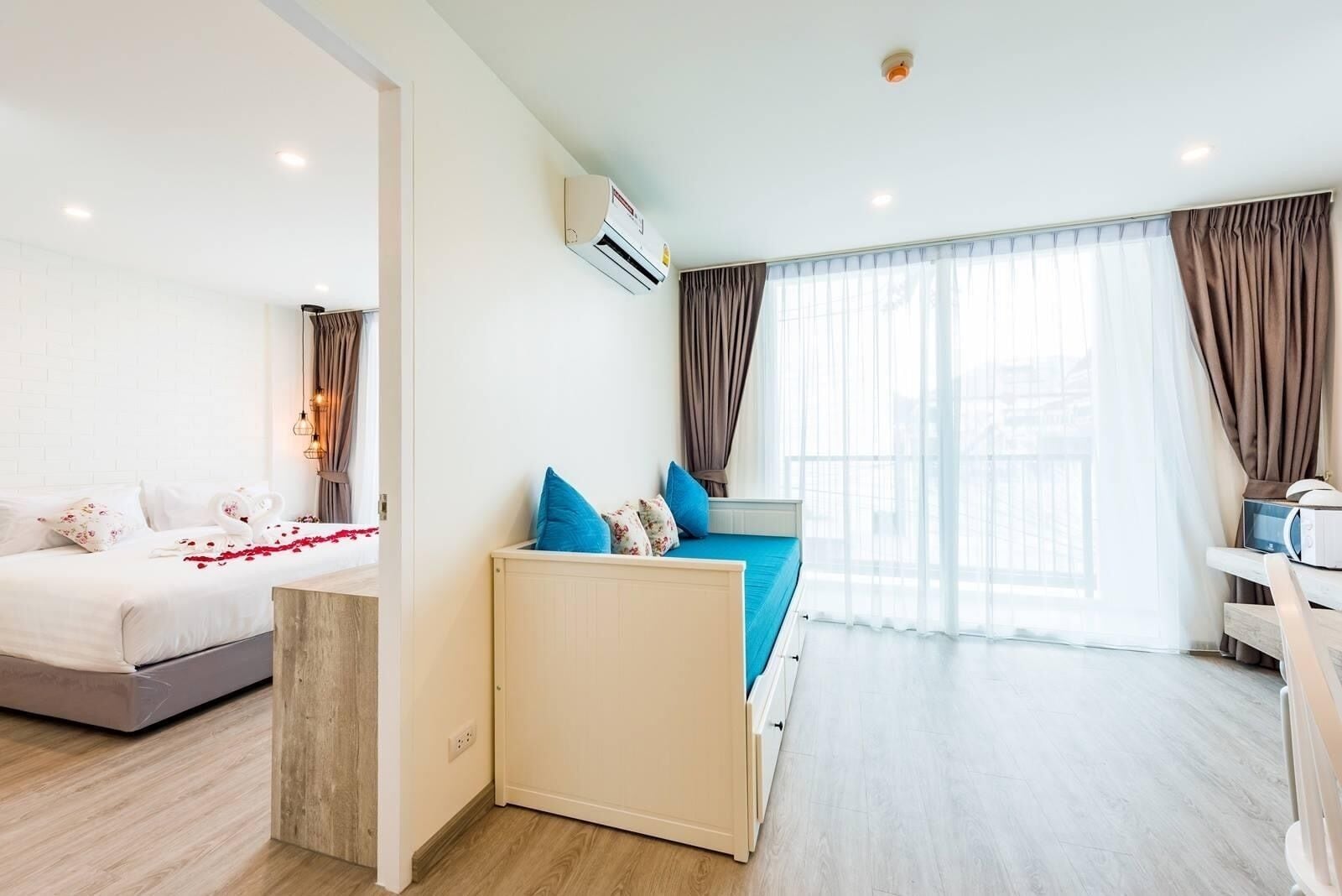 Habitación de hotel con cama, sofá, escritorio y un amplio ventanal con cortinas.