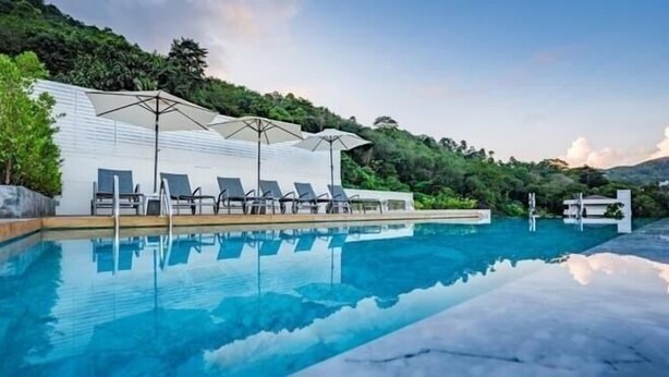 A swimming pool with lounge chairs and umbrellas, surrounded by greenery and hills. - LullaBella Hotel Patong (Patong)