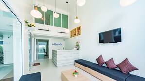 A modern hotel lobby with a reception desk, seating area, and a TV mounted on the wall. - LullaBella Hotel Patong (Patong)