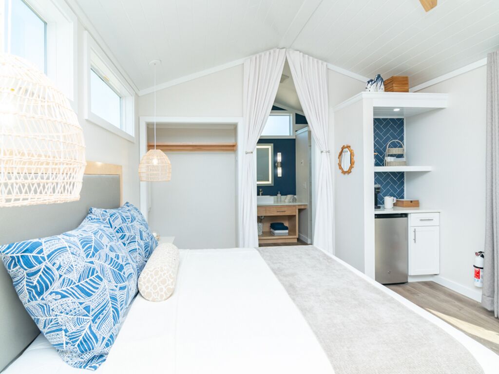 A bedroom with a bed, a bedside table, a hanging light fixture, a wardrobe, and a bathroom visible through an open door.