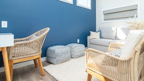 Une pièce avec un mur bleu, un canapé blanc, deux fauteuils en osier, une petite table blanche et un tapis à motifs.