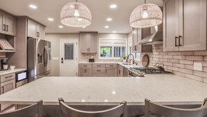 Una cocina moderna con una isla grande, electrodomésticos de acero inoxidable e iluminación colgante.