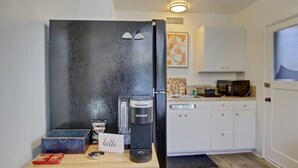 A compact kitchen with a black refrigerator, a coffee maker, and a small coffee pod dispenser. There is a wooden counter with a card that reads "hello". - NorthEnd Stylish Home Near Hiking Trails & BSU (Boise)