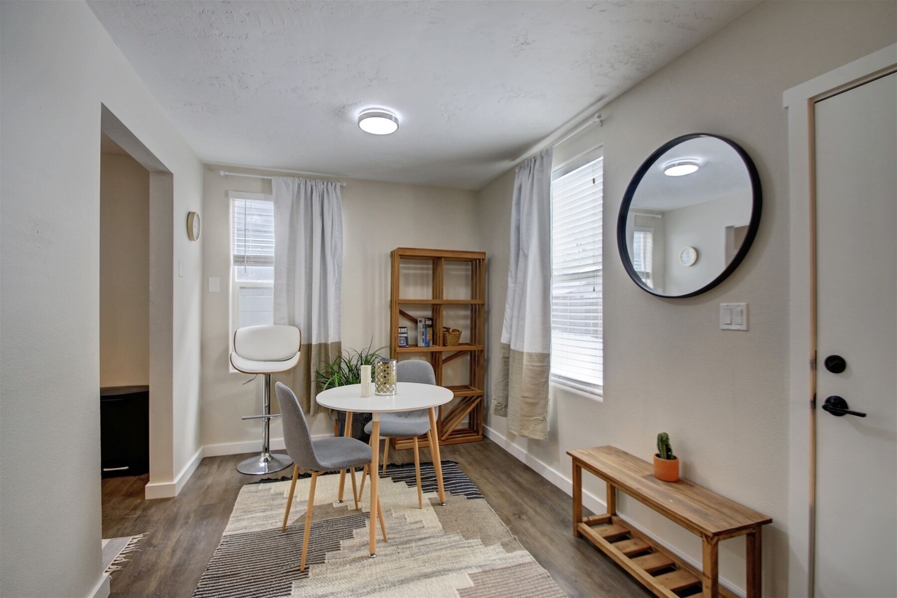 Ett kompakt bostadsutrymme med en matplats, en liten bokhylla och en spegel på väggen.