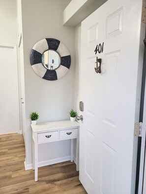 A hallway with a white door marked "401", a white console table with two drawers, a small potted plant, and a round mirror with a black and white design. - Lakefront Corner Condo with Boat Slip - Stunning Views - Pool - Laundry (Osage Beach)
