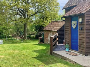 A rustic wooden building with a blue door, surrounded by a well-maintained lawn and large trees. - 1 bedroom accommodation in Battle (Battle)
