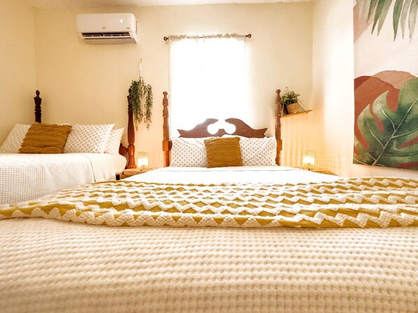 Une chambre avec un grand lit, une fenêtre avec un rideau, un climatiseur fixé au mur et une plante.