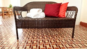 Un canapé en osier avec des coussins rouges et une serviette blanche, posé sur un sol à motifs.