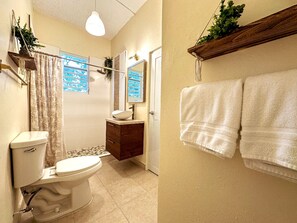 Une salle de bain avec des toilettes, un lavabo et un miroir. Des serviettes sont accrochées au mur et une plante est posée sur une étagère.