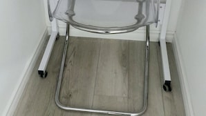 Un meuble d’angle pour le rangement, doté d’une étagère transparente et d’une étagère inférieure, fixé à un mur blanc avec un plancher en bois.