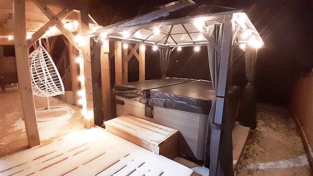 Une structure en forme de tente, avec un matelas à l’intérieur, entourée d’une ossature en bois et illuminée par des guirlandes lumineuses.