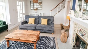Un salón con sofá gris, mesa de centro de madera, alfombra estampada y chimenea con baldosas decorativas.