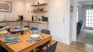 Una cocina moderna con armarios blancos, una mesa de comedor de madera dispuesta con platos y cubiertos, y una cafetera.