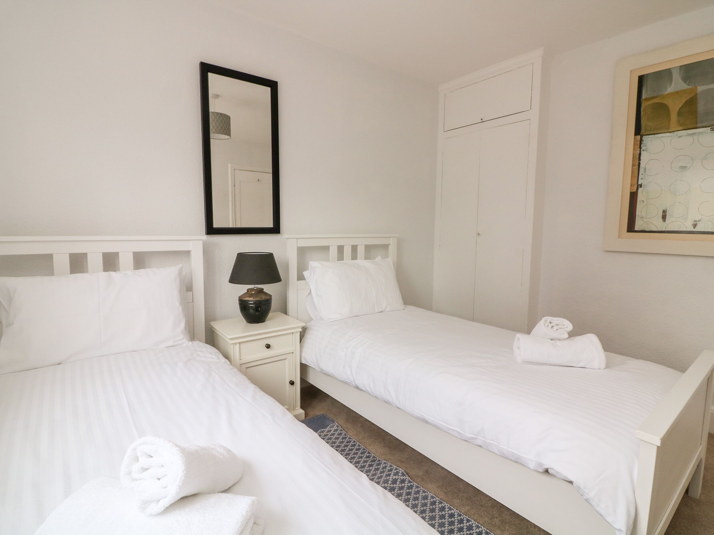 Une chambre d’hôtel avec deux lits simples, une table de chevet avec une lampe, un miroir et une armoire.