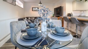 A modern dining area with a glass table set for four, a sofa, and a kitchen in the background. - Little Haven (Frinton-on-Sea)