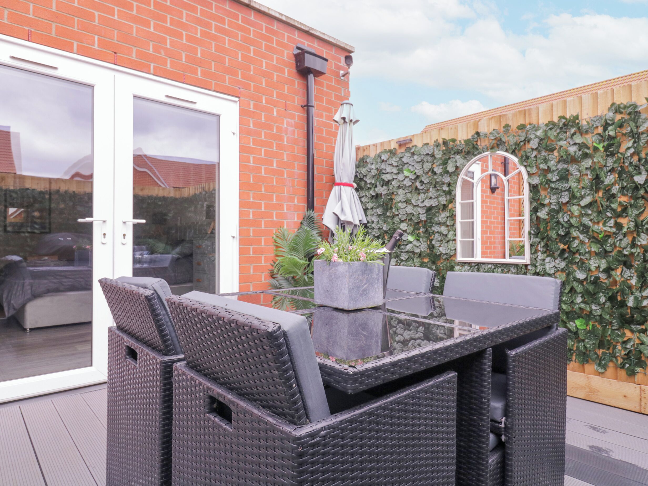 An outdoor patio area with wicker furniture, a glass door leading to a patio, and a brick wall with ivy.