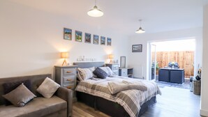 A bedroom with a bed, bedside tables, a sofa, and a view of the outside. - Little Haven (Frinton-on-Sea)
