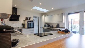 A modern kitchen with a built-in oven, a coffee machine, and a large island with a black countertop. - Little Haven (Frinton-on-Sea)