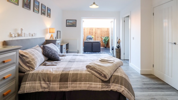 A bedroom with a bed, bedside table, lamp, and wall-mounted power outlets. - Little Haven (Frinton-on-Sea)
