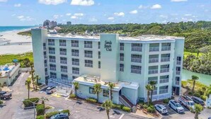 A multi-story hotel with a central tower labeled "Sands Beach Club," surrounded by a parking lot and palm trees. - Sands Beach Club | Ocean & Pool View | Amenities! (Myrtle Beach)