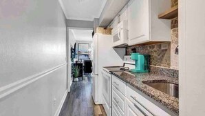 A narrow hallway leading to a kitchen with white cabinets, a granite countertop, and a stone backsplash. - Sands Beach Club | Ocean & Pool View | Amenities! (Myrtle Beach)