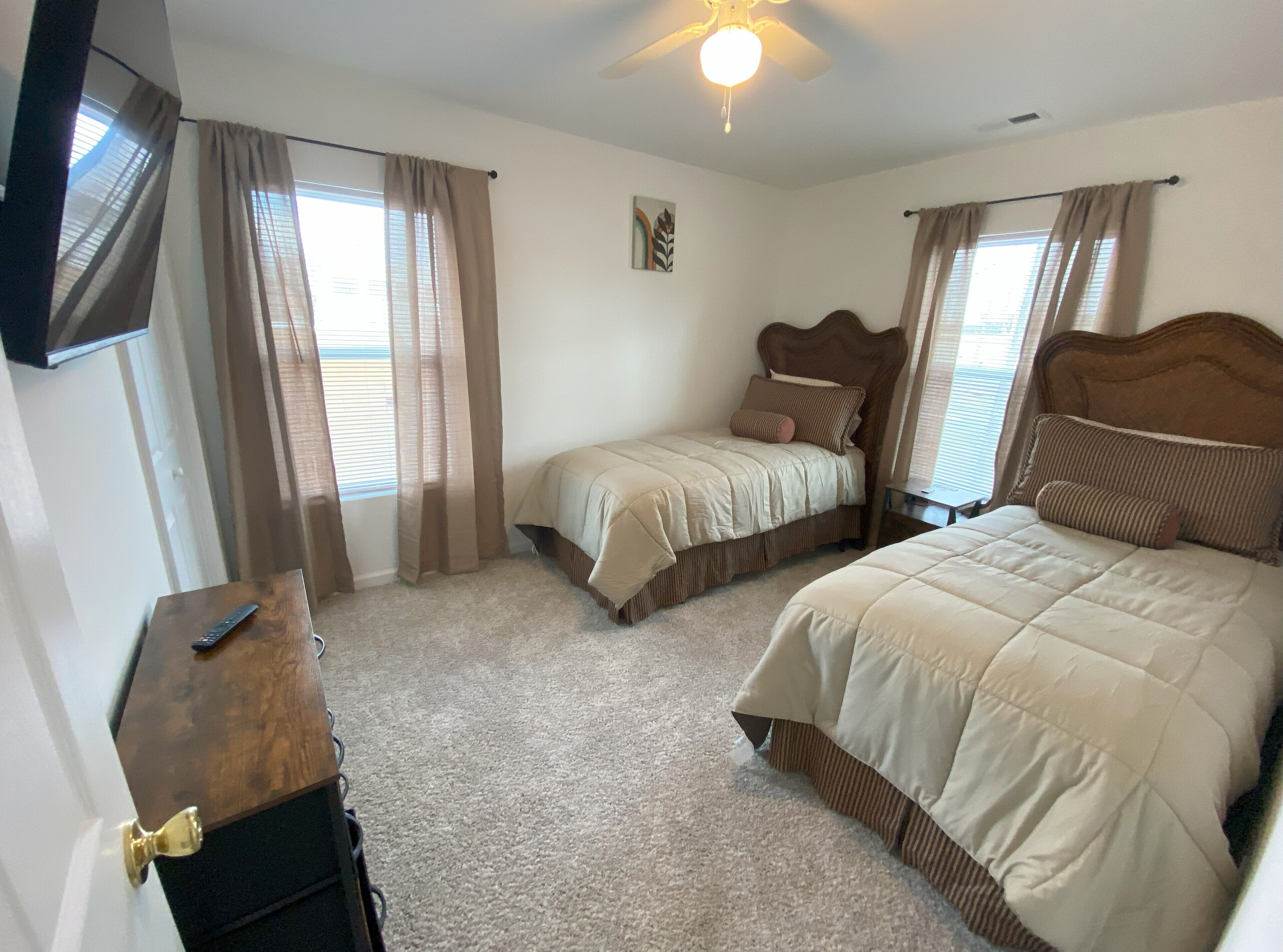 A bedroom with two beds, a ceiling fan, and a TV mounted on the wall.