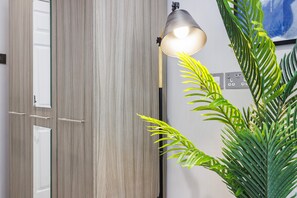 A wooden wardrobe with a mirror, a lamp, and a potted plant. - Quality Spitalfields Accommodations (London)