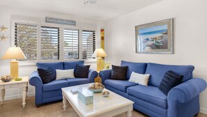 A living room with two blue sofas, a white coffee table, and a painting of a beach scene. - 2nd Floor Studio for 4, Pool, 300 Yds to the Beach + Free Attraction Tickets! (Santa Rosa Beach)