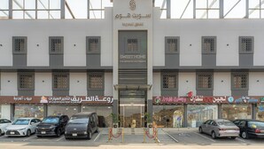 A multi-story building with a central entrance, several shops on the ground floor, and parked cars in front. - Sweet Home Serviced Apartments (Jeddah)