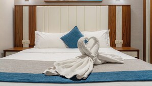 A neatly made bed with a towel shaped like a swan, a blue pillow, and a painting of a beach scene above it. - Sweet Home Serviced Apartments (Jeddah)