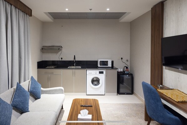 Un espace de vie compact comprenant un canapé, une table basse, un lave-linge, un four à micro-ondes, une télévision et une petite kitchenette.