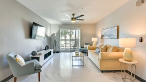 A modern living room with a sofa, armchair, TV, and ceiling fan. - Summer Getaway: Destin Condo by Golf & Dining (Destin)
