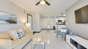 A modern living room with a sofa, coffee table, and a dining area in the background. - Summer Getaway: Destin Condo by Golf & Dining (Destin)