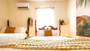 Quarto aconchegante com uma cama grande, duas camas menores, uma planta pendurada e uma janela com cortinas.